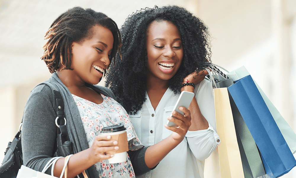 Two smiling shoppers checking a phone together, seeing how a brand strategy consultant helps a product stand out
