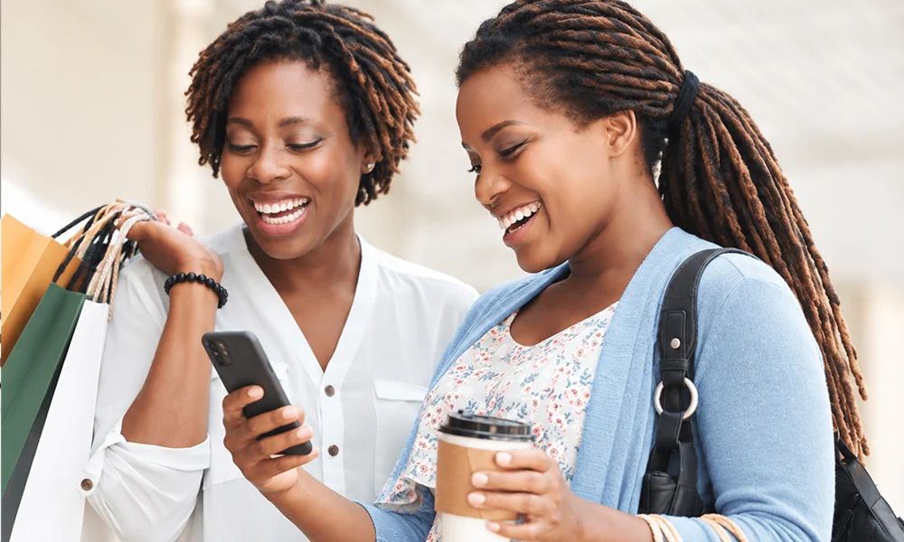 Two smiling shoppers checking a phone together, seeing how a brand strategy consultant helps a product stand out